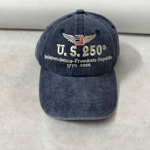 May include: A navy blue baseball cap with embroidered text and a patriotic design. The cap features the text "U.S. 250th Independence-Freedom-Republic 1776-2026" in white thread, along with an American flag and wings.