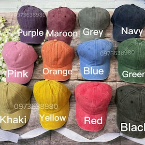May include: A collection of baseball caps in various colors, including purple, maroon, grey, navy, pink, orange, blue, green, khaki, yellow, red, and black. Each cap has a curved brim and a top button. The image also displays the phone number 973638980.