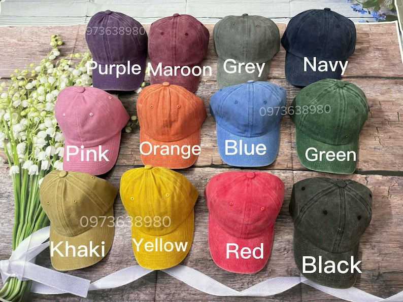 May include: A collection of baseball caps in various colors, including purple, maroon, grey, navy, pink, orange, blue, green, khaki, yellow, red, and black. Each cap has a curved brim and a top button. The image also displays the phone number 973638980.
