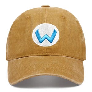 May include: A tan baseball cap with a curved brim. The cap features a white circular patch on the front with a blue "W" logo embroidered in the center. The cap is made of a soft, worn material.