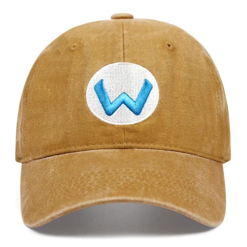 May include: A tan baseball cap with a curved brim. The cap features a white circular patch on the front with a blue "W" logo embroidered in the center. The cap is made of a soft, worn material.