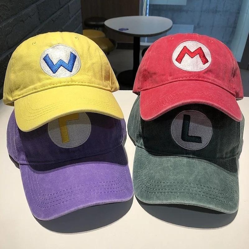 May include: Four baseball caps in yellow, red, purple, and green. Each cap has a different letter embroidered on the front: W, M, F, and L. The caps are stacked on top of each other.
