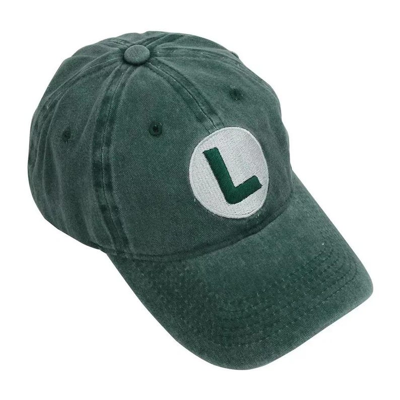 May include: A dark green baseball cap with a curved brim. The cap features a white circular patch with a green "L" on the front. The cap is made of a soft, worn material.