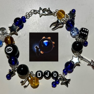 May include: A beaded bracelet with charms, including a black 8-ball, dice, a guitar, and star shapes. The bracelet features blue and black beads, with the letters "DJO" spelled out. A small image of a magic 8-ball is also included.