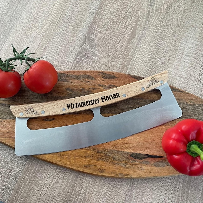 Może przedstawiać: N&oacute;ż do pizzy ze stali nierdzewnej z zakrzywionym ostrzem i jasnym drewnianym uchwytem. Uchwyt jest wygrawerowany napisem "Pizzameister Florian" i posiada małe ikony kawałk&oacute;w pizzy na obu końcach, przymocowane za pomocą czterech metalowych nit&oacute;w.