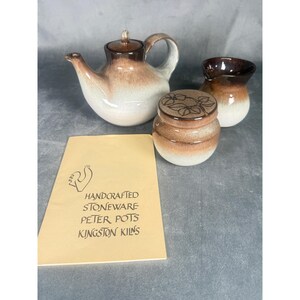 May include: A handcrafted stoneware tea set by Peter Pots, featuring a teapot, creamer, and lidded jar. The set has a brown and white gradient design. The included card reads "HANDCRAFTED STONEWARE PETER POTS KINGSTON KILNS".