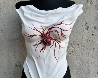 May include: White bodysuit with a draped neckline, featuring a detailed anatomical heart and vein design in red. The bodysuit is displayed on a black mannequin, showcasing a unique and artistic garment.