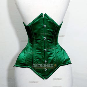 May include: A dark green satin corset with a structured design. The corset features a series of metal clasps down the front and is displayed on a mannequin. The text "DECRUMEX CUSTOM RIDING GEAR & APPAREL" is visible.