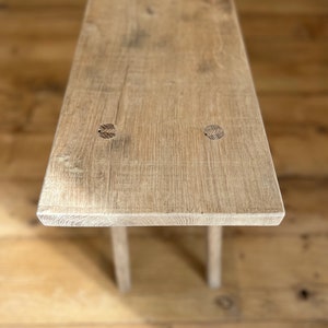 May include: A rustic wooden bench with a light brown finish. The bench has a simple design with two legs and a rectangular top. The top of the bench has two visible knots.