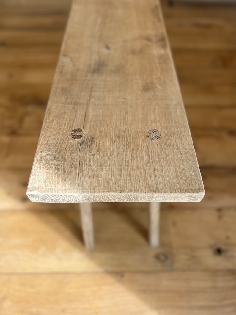 May include: A rustic wooden bench with a light brown finish. The bench has a simple design with two legs and a rectangular top. The top of the bench has two visible knots.