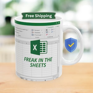 Può includere: Tazza da caffè bianca con un design di foglio di calcolo Microsoft Excel verde. Il foglio di calcolo mostra il testo "FREAK IN THE SHEETS" e il logo Excel.