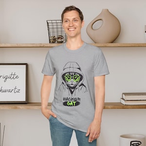 Könnte beinhalten: Ein graues T-Shirt mit einer schwarz-weißen Illustration einer Katze, die eine Kapuzenjacke und grüne Sonnenbrillen trägt. Der Text "Hacker Cat" ist in Grün unter der Katze aufgedruckt.