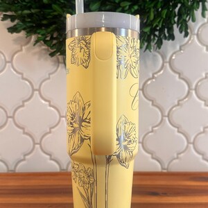 May include: A yellow stainless steel tumbler with a black and white floral design. The tumbler has a lid and a straw.