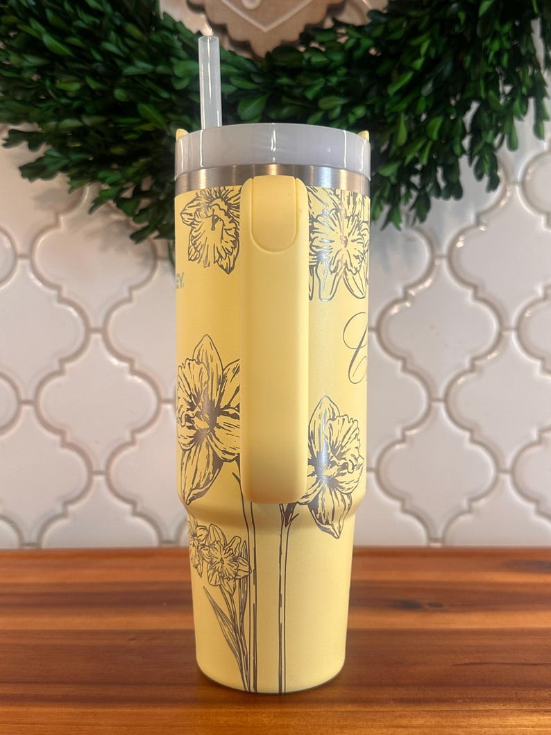 May include: A yellow stainless steel tumbler with a black and white floral design. The tumbler has a lid and a straw.