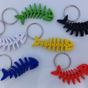 May include: Six colourful fish bone keyrings with silver key rings. The keychains are made of plastic and are shaped like fish skeletons. The colours are green, black, white, yellow, blue, and red.