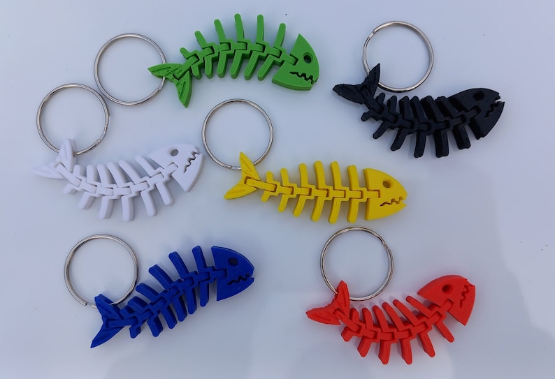 May include: Six colourful fish bone keyrings with silver key rings. The keychains are made of plastic and are shaped like fish skeletons. The colours are green, black, white, yellow, blue, and red.
