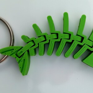 May include: A green plastic fish skeleton keyring. The skeleton is articulated and has a silver key ring.