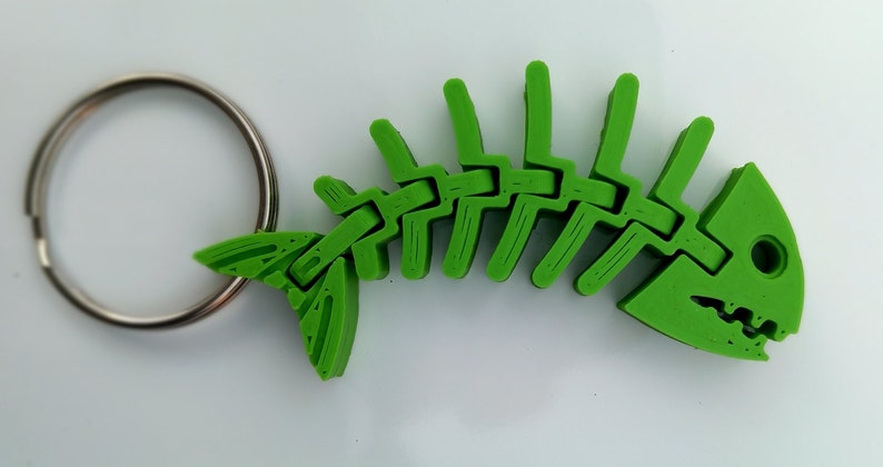 May include: A green plastic fish skeleton keyring. The skeleton is articulated and has a silver key ring.