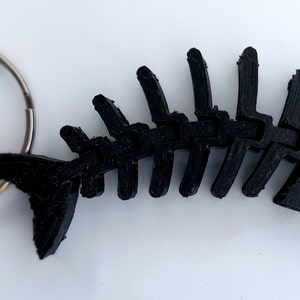May include: A black plastic fish skeleton keychain. The skeleton is detailed and has a small ring attached to the tail.