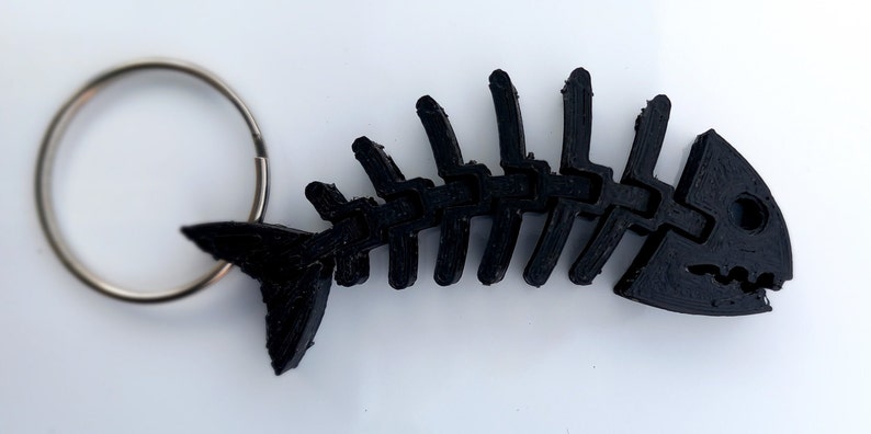May include: A black plastic fish skeleton keychain. The skeleton is detailed and has a small ring attached to the tail.