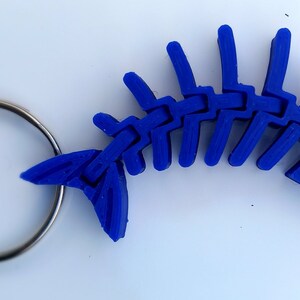 May include: A blue plastic fish skeleton keyring. The skeleton is detailed and realistic, with a silver key ring attached.