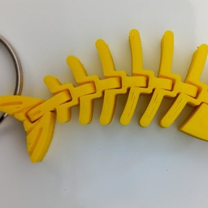 May include: A yellow plastic fish skeleton keyring. The skeleton is detailed and has a realistic shape. The keyring is attached to a silver metal ring.