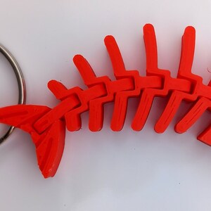 May include: A bright red plastic fish skeleton keychain. The fish skeleton is detailed and has a silver key ring attached.