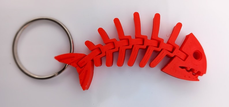 May include: A bright red plastic fish skeleton keychain. The fish skeleton is detailed and has a silver key ring attached.