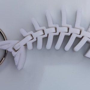May include: White plastic fish skeleton keyring with a silver key ring. The skeleton is articulated and has a detailed head with teeth.