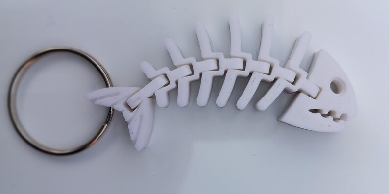 May include: White plastic fish skeleton keyring with a silver key ring. The skeleton is articulated and has a detailed head with teeth.