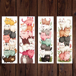 May include: Four vertical bookmarks featuring stacks of cartoon cats in various colors. Each bookmark showcases a different arrangement of cats, including orange, pink, gray, and black, with floral accents. The background is a wooden surface.