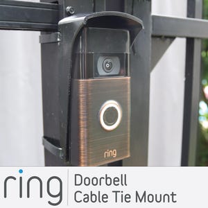 May include: A black and bronze Ring doorbell with a black weather shield mounted on a black metal fence. The doorbell has a button and a camera lens. The text "ring" is printed on the doorbell.