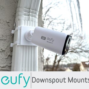 May include: A white security camera mounted on a white downspout mount. The camera has a black lens and the text "2K eufy SECURITY". The image also includes the text "eufy Downspout Mounts".