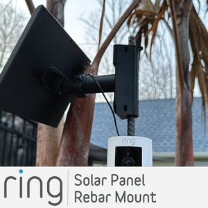 May include: A black solar panel mounted to a rebar post with a white Ring security camera attached. The text "ring" is visible on the camera.