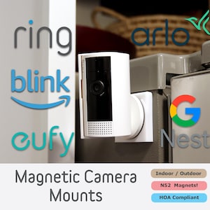 May include: A white magnetic camera mount with a black camera lens. The mount is attached to a white surface. The image includes the logos for Ring, Blink, Eufy, Arlo, and Google Nest.