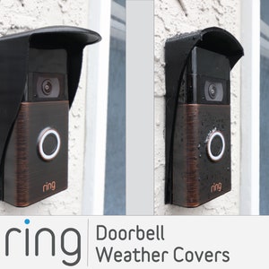 May include: Two Ring doorbells with black weather covers installed on a white wall. The doorbells are bronze colored with a black camera lens and a black button. The text "ring" is printed on the bottom of each doorbell.
