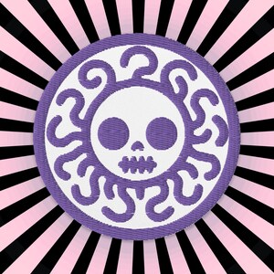 May include: Purple and white embroidered patch with a skull design. The skull has two large eyes and a toothy grin. The skull is surrounded by a swirling design.