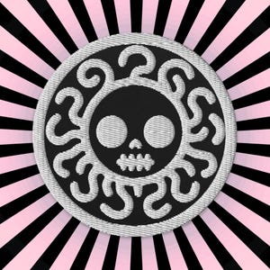 Può includere: Un teschio ricamato bianco su sfondo nero con un bordo circolare bianco. Il teschio è circondato da un motivo bianco a spirale.
