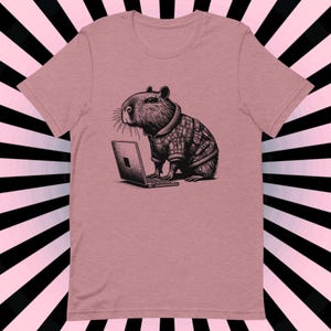 May include: A pink t-shirt with a black and white illustration of a capybara wearing a plaid shirt and using a laptop computer.