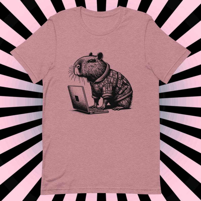 May include: A pink t-shirt with a black and white illustration of a capybara wearing a plaid shirt and using a laptop computer.