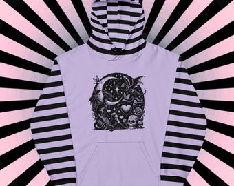 May include: A lavender hoodie with black and white striped sleeves. The front of the hoodie features a black and white graphic of a dragon, a crescent moon, and other mystical elements.