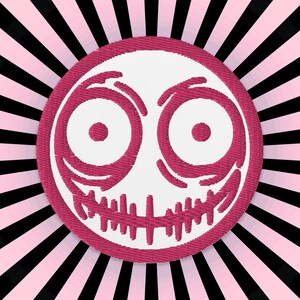 Peut inclure: Un patch brodé rose et blanc avec un visage souriant. Le visage a deux grands yeux avec des pupilles roses et un large sourire aux dents.
