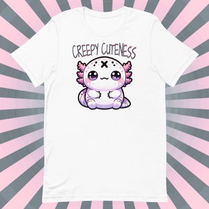 Op de afbeelding: Wit T-shirt met een roze en witte axolotl-illustratie en de tekst "Creepy Cuteness" gedrukt op de voorkant.