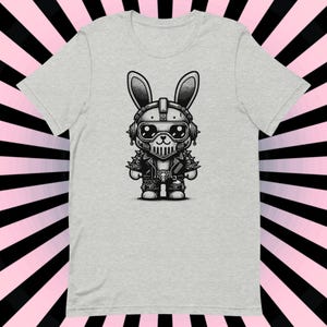 May include: A light gray t-shirt featuring a black and white illustration of a rabbit wearing a motorcycle helmet, jacket, and boots. The rabbit has large eyes and is in a biker-punk style.