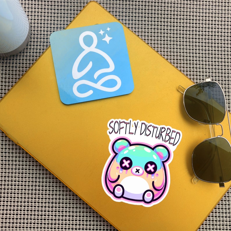 Może przedstawiać: Ż&oacute;łte tło z naklejką przedstawiającą pastelowo-niebieską i r&oacute;żową postać z kresk&oacute;wki z tekstem "Softly Disturbed" nad nią. Jest niebieska naklejka z białym konturem osoby siedzącej w pozycji medytacyjnej z gwiazdami nad nią.