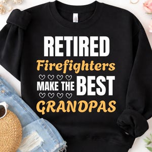 Peut inclure: Sweat-shirt noir avec l'inscription "RETIRED Firefighters MAKE THE BEST GRANDPAS" en lettres blanches et jaunes. Le motif comprend des symboles de cœur. Le sweat-shirt est plié sur une surface en denim bleu clair.
