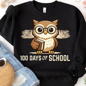 Peut inclure: Sweat-shirt noir avec un dessin de hibou portant des lunettes et tenant un livre. Le hibou est brun et beige avec un bec et des pieds jaunes. Le texte "100 DAYS OF SCHOOL" est imprimé en blanc en dessous.