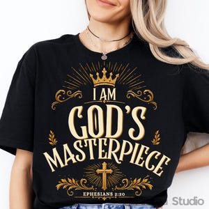 Peut inclure: Un t-shirt noir avec un motif graphique doré comprenant une couronne en haut, le texte "I AM GOD'S MASTERPIECE" en grandes lettres, une croix sous le texte et la citation "EPHESIANS 2:20" en bas avec des ornements décoratifs.