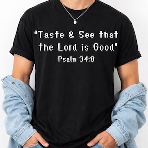 Peut inclure: T-shirt noir avec le texte "Taste & See that the Lord is Good" et Psaume 34:8 imprimé en blanc. Le t-shirt est porté avec une veste en jean et un collier argenté.