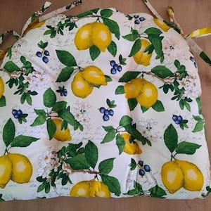 May include: White cushion with a lemon and floral pattern. The cushion has ties on the corners.